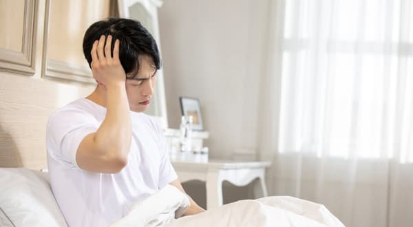 침대에 걸터앉아 머리를 감싸쥐고 있는 사람